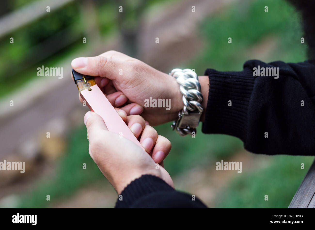 Close-up di persona a mano azienda sigaretta elettronica, con sfondo verde e un orologio di argento in mano Foto Stock