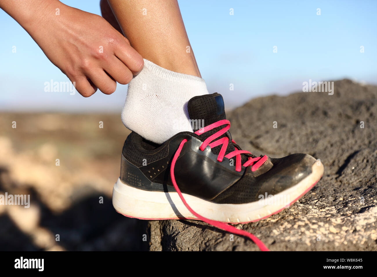 Runner mettendo sul fitness e scarpe running Scarpe closeup all'aperto su sfondo di montagna. Atleta femminile ottenere pronto per la maratona di preparare i suoi piedi sul sentiero esegui. Foto Stock