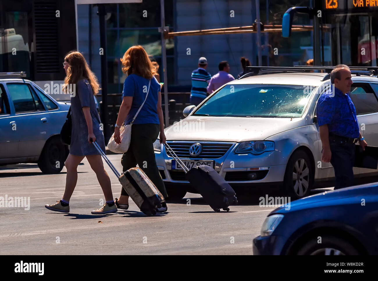 Bucarest, Romania - 07 agosto 2019: due turisti le donne che trasportano le valigie sono attraversando la strada di fronte a qualche auto in una giornata calda in centro a Buc Foto Stock