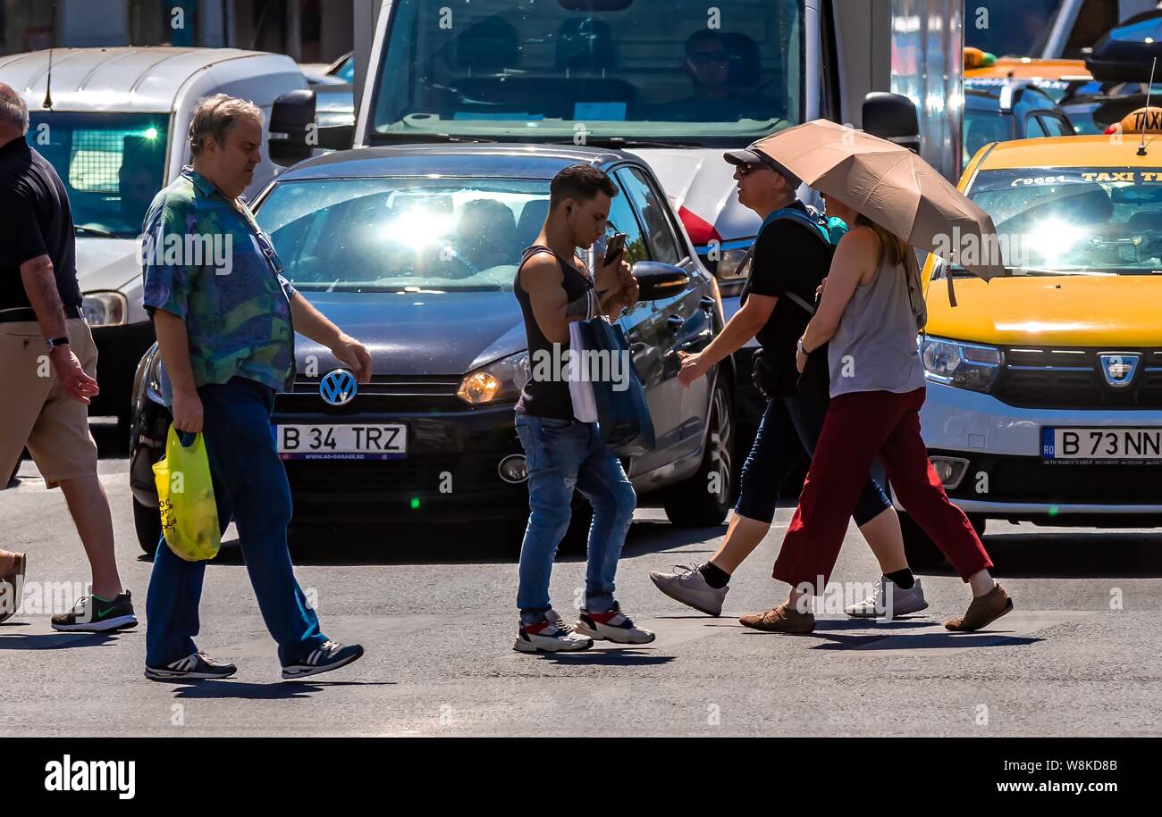 Bucarest, Romania - 07 agosto 2019: due donne i turisti che indossa il cappello e parasol stanno attraversando la strada di fronte a qualche auto in una giornata calda in downtow Foto Stock