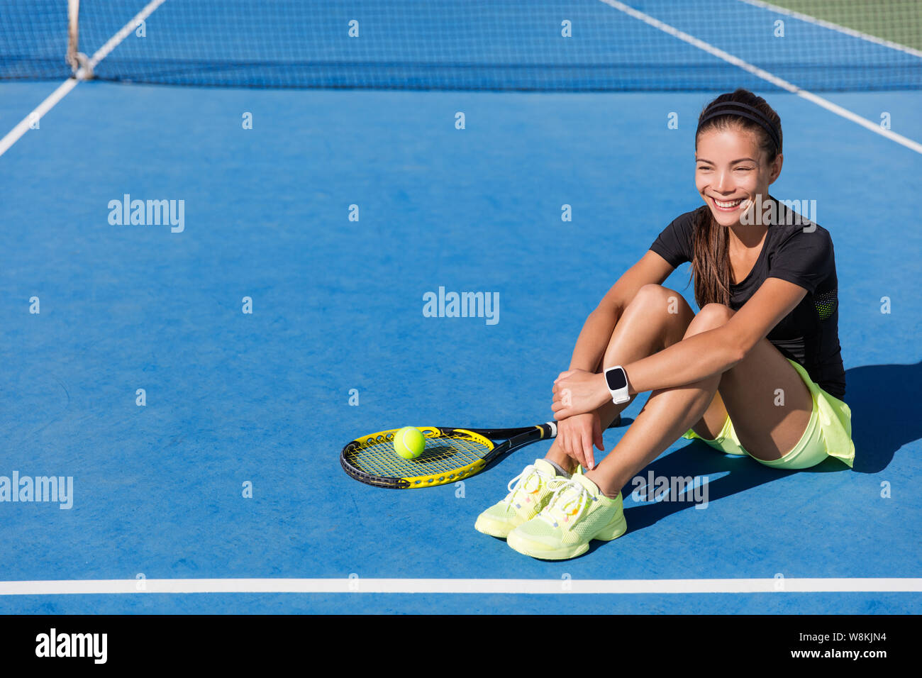 Giocatore di Tennis donna che indossa lo sport smartwatch. Bellissimo sport atleta ritratto in appoggio su blu outdoort cemento rilassante con felice wearable tech orologio da polso per attività tracker su allenamento fitness. Foto Stock