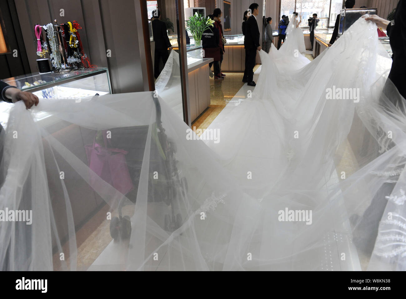 Un modello che indossa un abito nuziale con un 101-metro-long tail trasportati dai membri del personale di un abito da sposa azienda pone per le foto e i video in un negozio Foto Stock