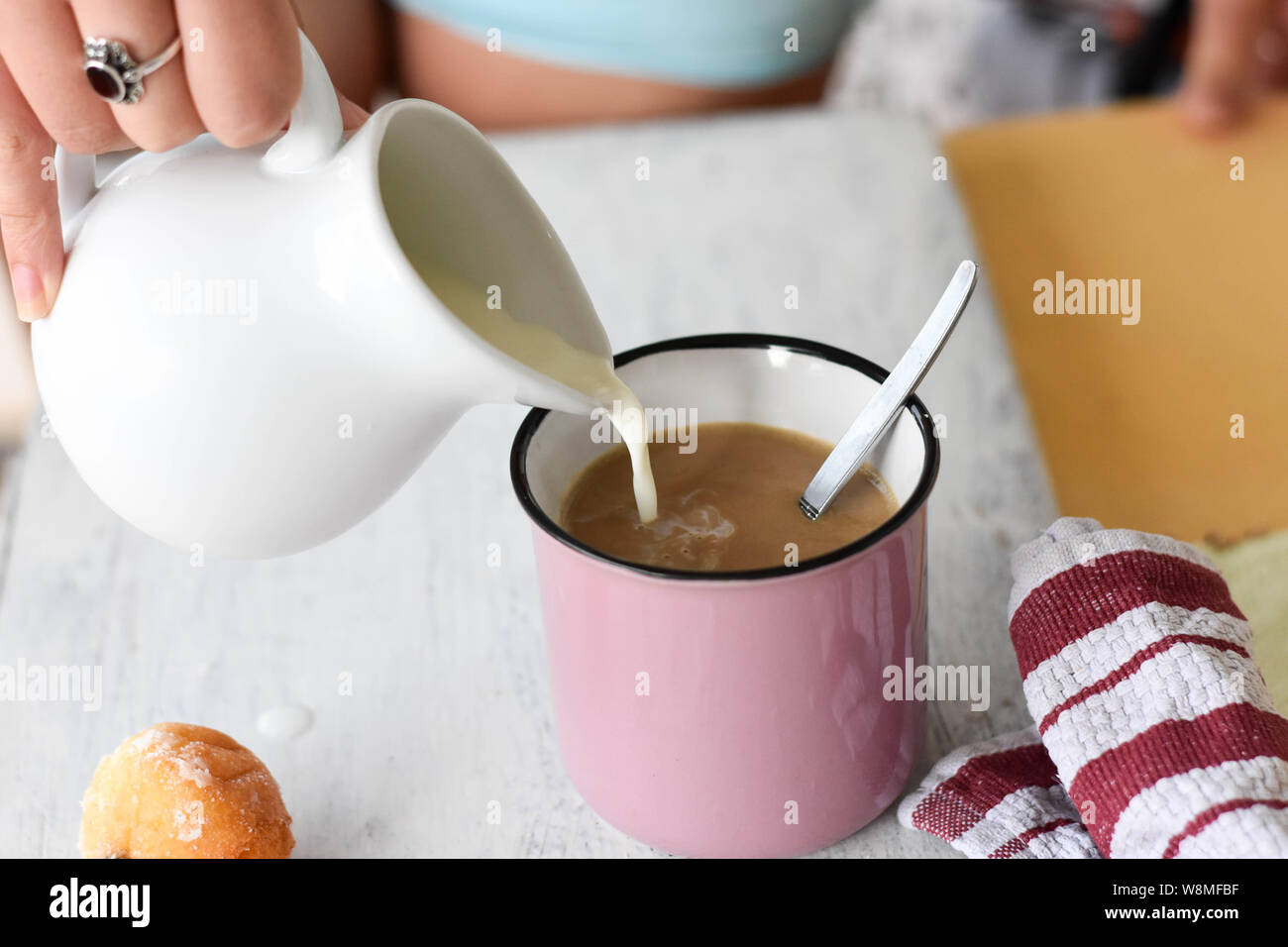 Donna versando il latte nella tazza da caffè/cappuccino/ tavolo per la prima colazione a partire da un giorno - Immagine Foto Stock