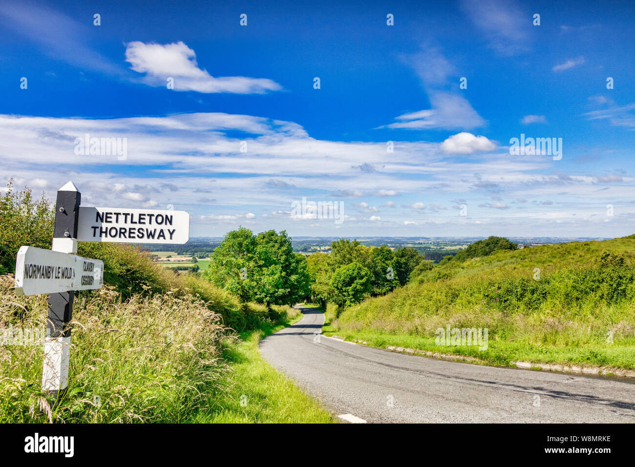 Una strada di campagna che corre attraverso il Lincolnshire Wolds, in una zona di straordinaria bellezza naturale e di un cartello per Nettleton Thoresway. Foto Stock
