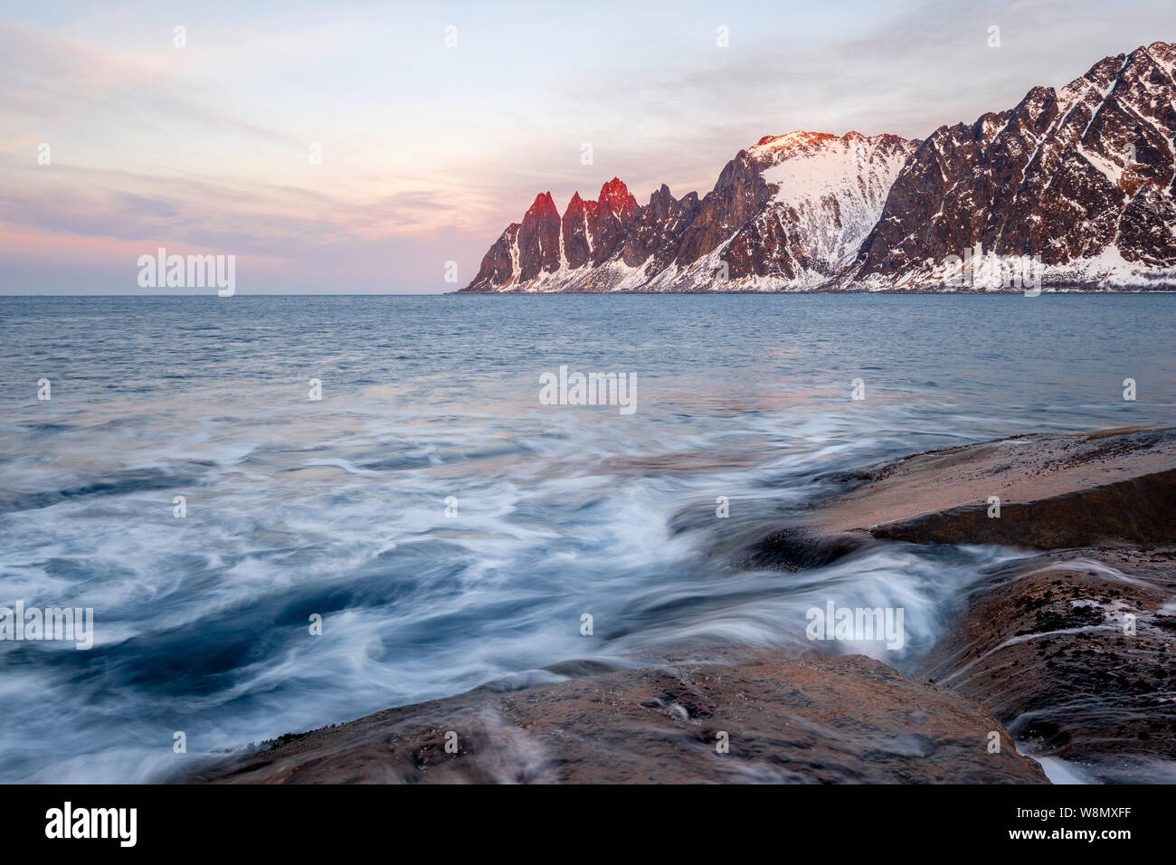 Vista su rocce colorate e le onde a Oksen innevate montagne su una serata artico , Tungeneset Devils ganascia Senja Norvegia Foto Stock