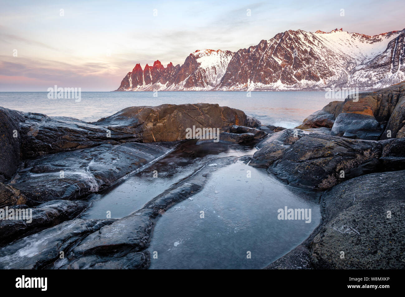 Vista su rocce colorate e rockpools a Oksen innevate montagne, Tungeneset Devils ganascia Senja Norvegia Foto Stock