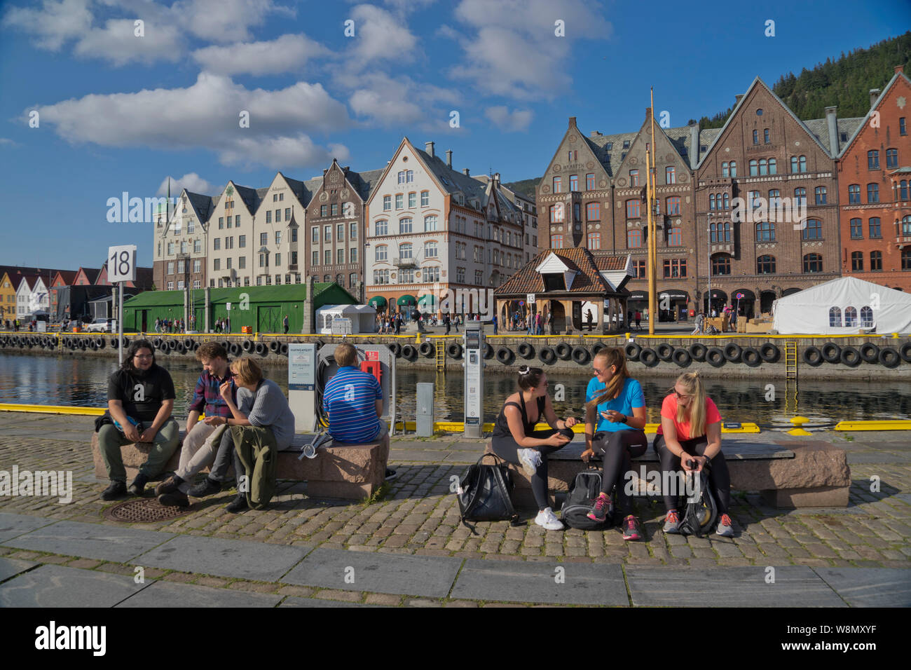 I turisti sedervi al sole in outdoor bar e caffetterie nel molo vecchio e tradizionali edifici in legno a Bryggen trimestre di Bergen, Norvegia Foto Stock