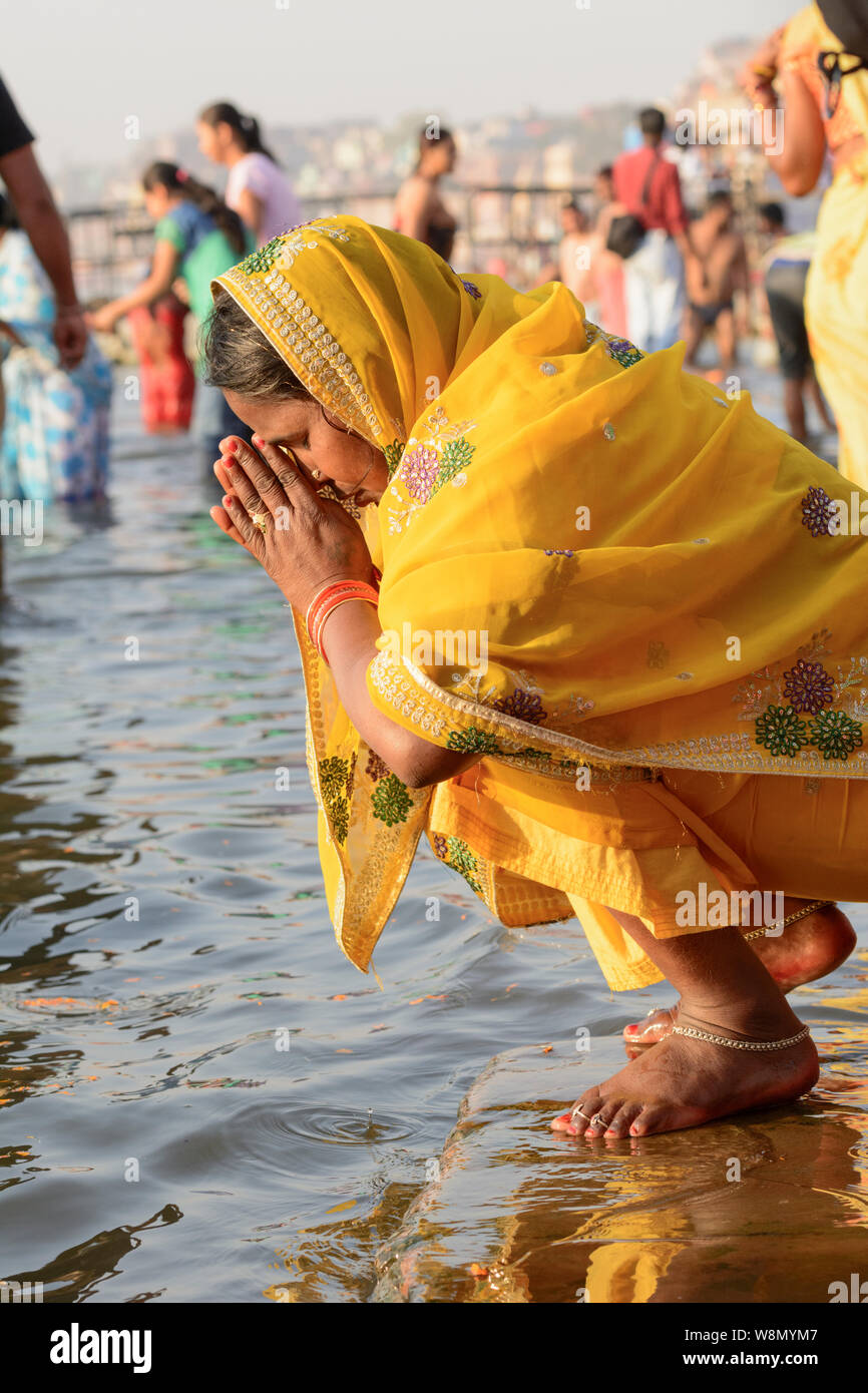 Un indiano donna Indù che indossa un giallo sari offre preghiere agli dèi sulle rive del Fiume Gange a Varanasi, Uttar Pradesh, India, Asia del Sud Foto Stock