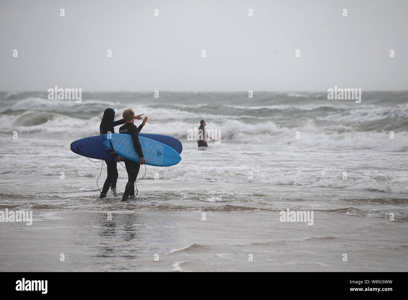 Due surfisti a piedi in mare sulla spiaggia di Bournemouth, come il Met Office ha messo gli avvisi di giallo in luogo per i temporali in Scozia e Irlanda del Nord e per i venti forti in tutto il Galles e la maggior parte dell'Inghilterra. Foto Stock