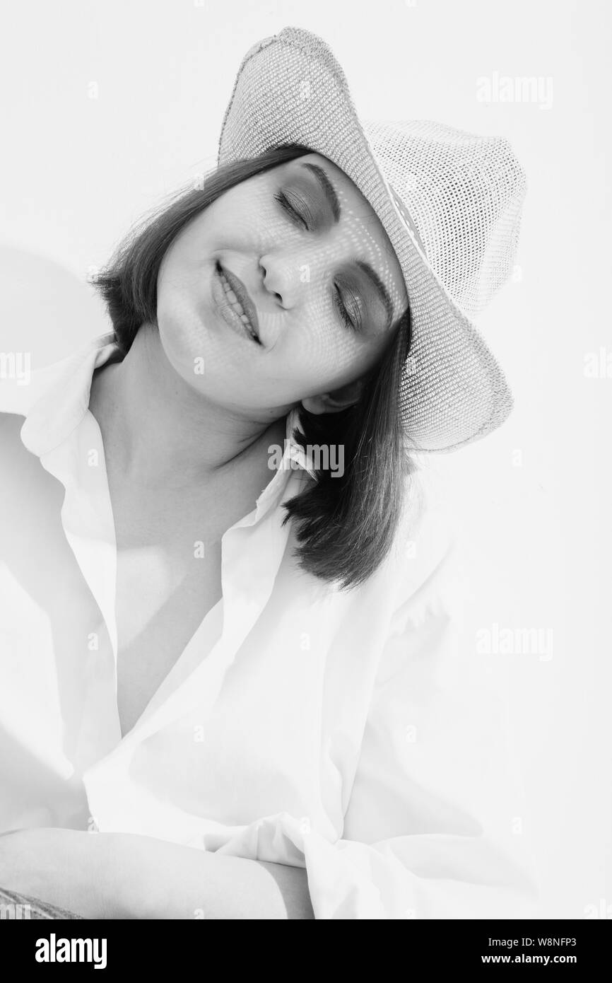 Felice giovane donna nel cappello sotto la luce del sole gli occhi chiusi relax, monocromatico Foto Stock