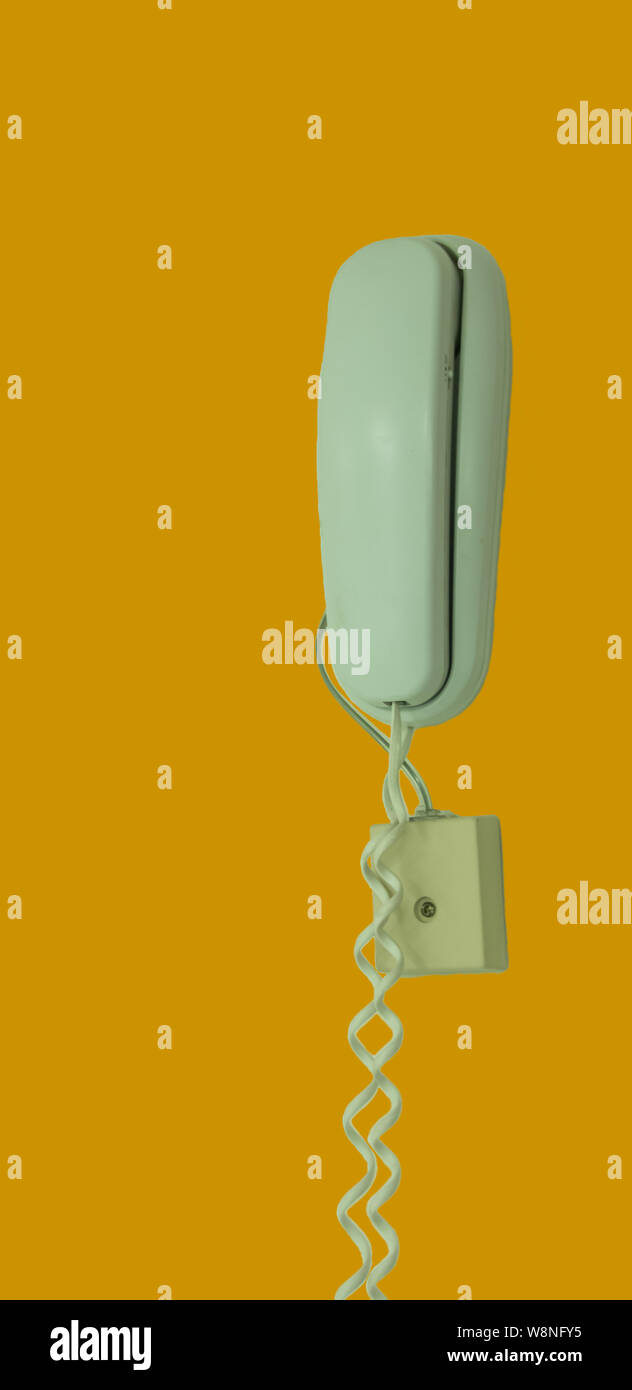 Il vecchio telefono appeso alla parete con uno sfondo giallo Foto Stock