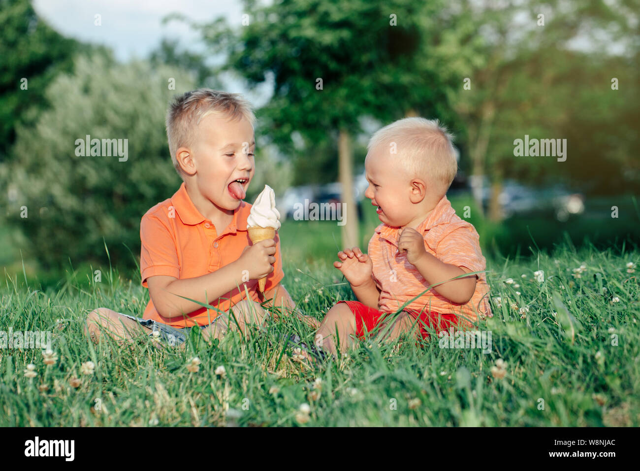Due caucasica bambini divertenti ragazzi fratelli seduti insieme la condivisione di mangiare un gelato. Il Toddler più giovane pianto del bambino e il fratello più anziano teasing lui. L Foto Stock
