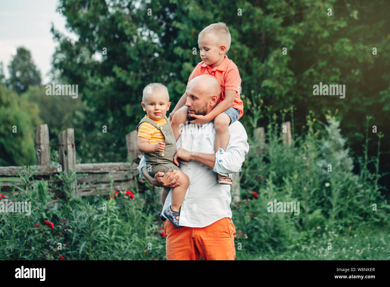 Padre caucasica abbracciando la riproduzione con figli i ragazzi nel parco sulla giornata d'estate. Papà tenendo il trasporto di bambini i bambini. Un autentico stile di vita toccante momento di gara. Foto Stock