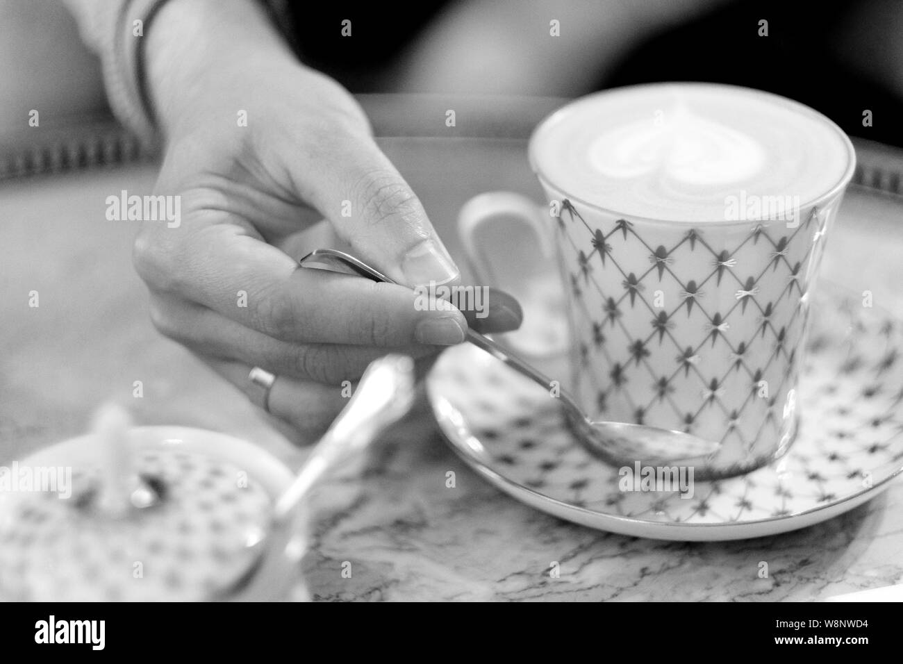 La mano di un uomo giovane con un cucchiaio sopra una tazza di caffè cappuccino in una tabella in un cafe Foto Stock