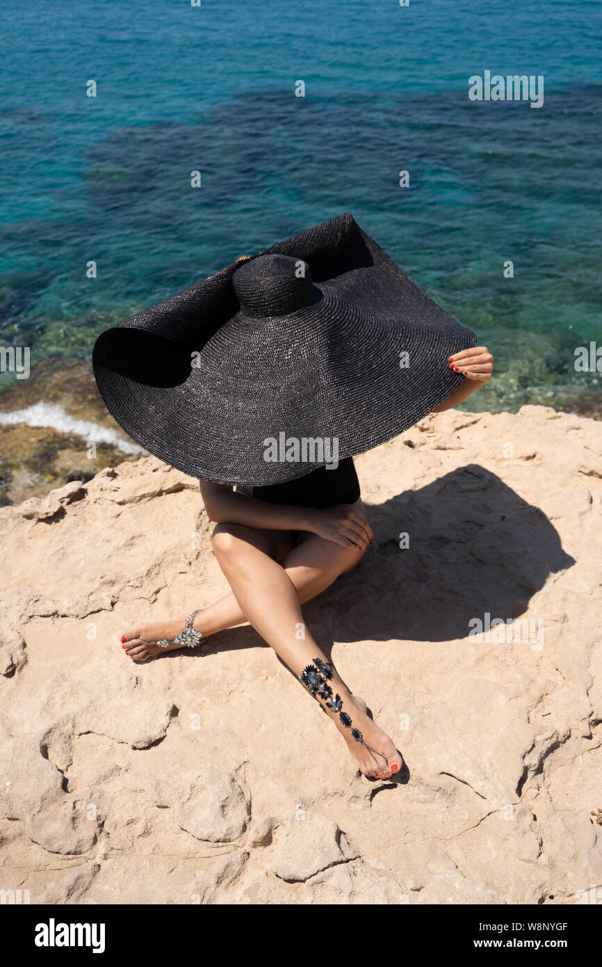 Modello con una larga tesa di paglia cappello estivo e gambe gioielli sul bordo del Cape Greco cliff (Cavo Greco, Capo Greco). Concetto di elegante vacanza estiva, Foto Stock