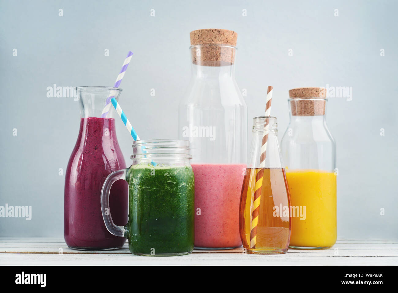 Arancione, verde e colorato di rosso frullati e succhi di frutta in vasetti di vetro su uno sfondo blu. Foto Stock