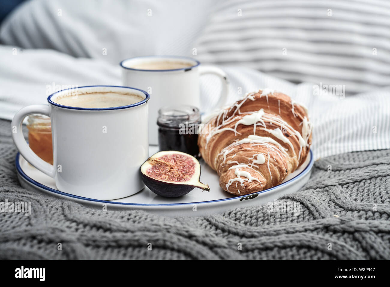 Vassoio con due tazze di caffè, diverse marmellate in vasetti e croissant sul letto al momento della colazione Foto Stock