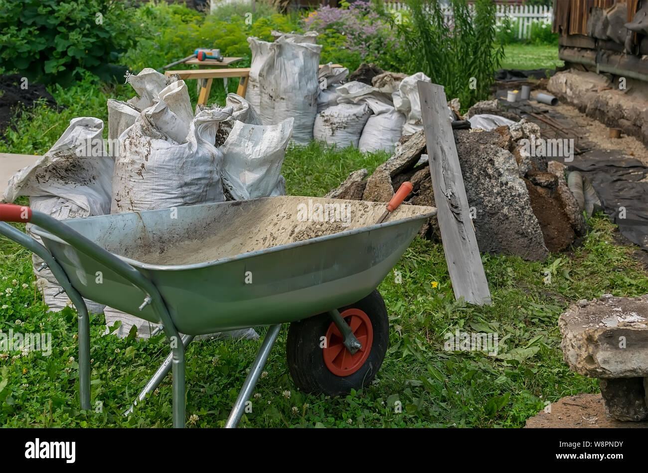 Rifiuti di costruzione, il carrello di trasporto e altri strumenti sono situati sul territorio di un giardino privato plot Foto Stock