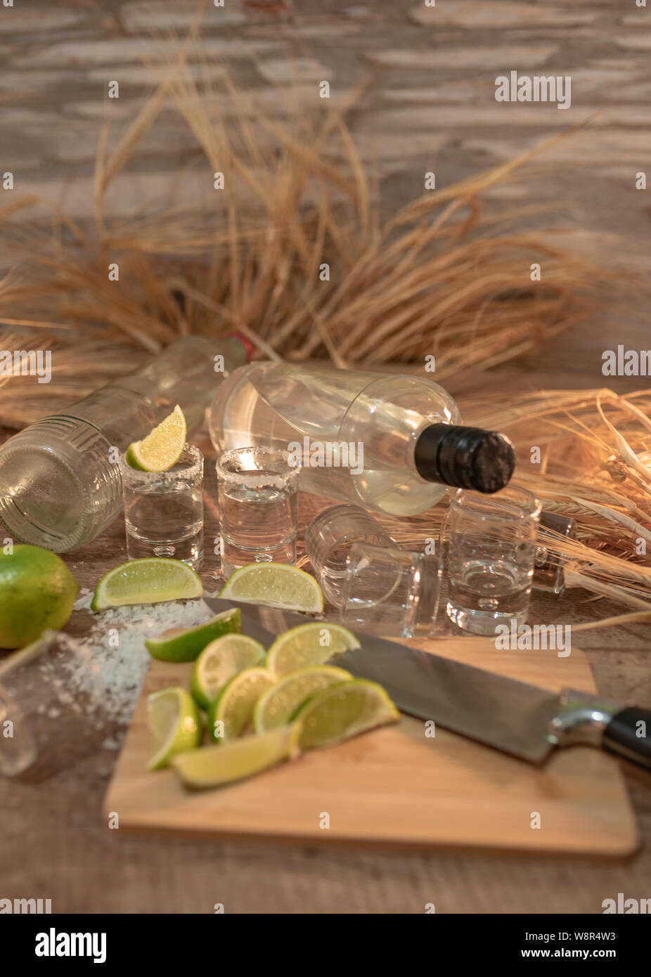 Dettaglio foto di due bottiglie di tequila di lusso, shot e molte fette di limone con picchi di grano sul tavolo di legno - immagine verticale Foto Stock