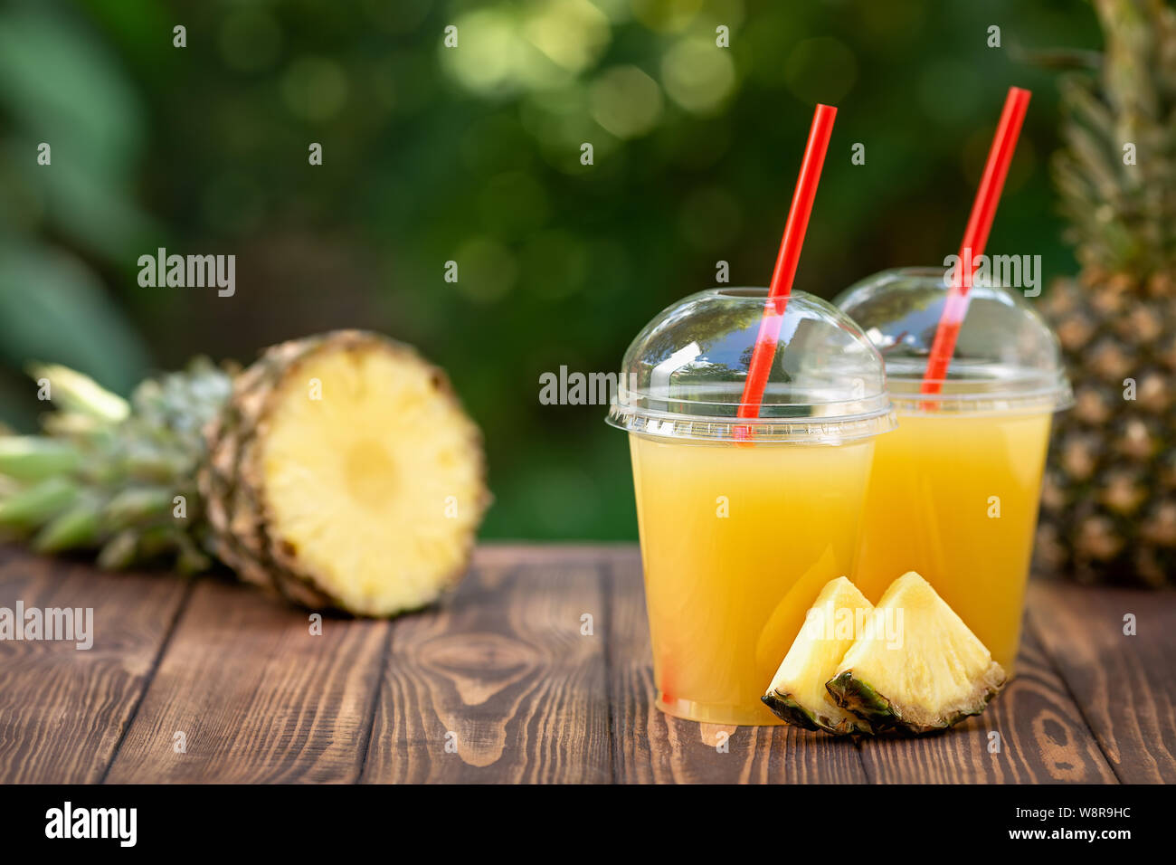 Ananas fresco succo in due in plastica monouso Tazze e aromi di frutta matura sul tavolo in legno all'esterno. Togliere il vetro con estate bevanda rinfrescante Foto Stock