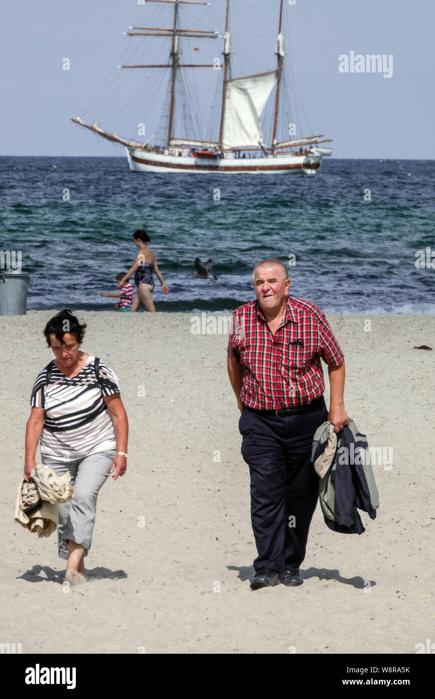 Germania Rostock, anziani, anziani che camminano sulla spiaggia, barca a vela sullo sfondo, spiaggia di Warnemunde, spiaggia di Ostsee coppia anziani Foto Stock