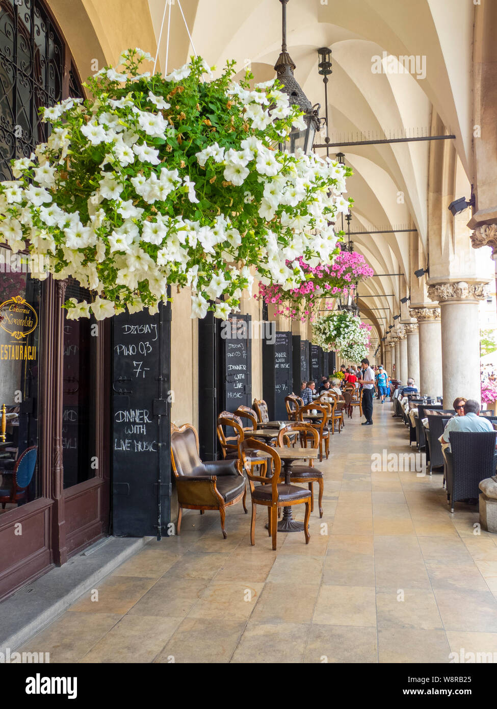 Cracovia, Poland-June 10,2015: coffee shop sotto i portici del panno hall di Cracovia con sedie di legno e appendere dei POT del fiore Foto Stock