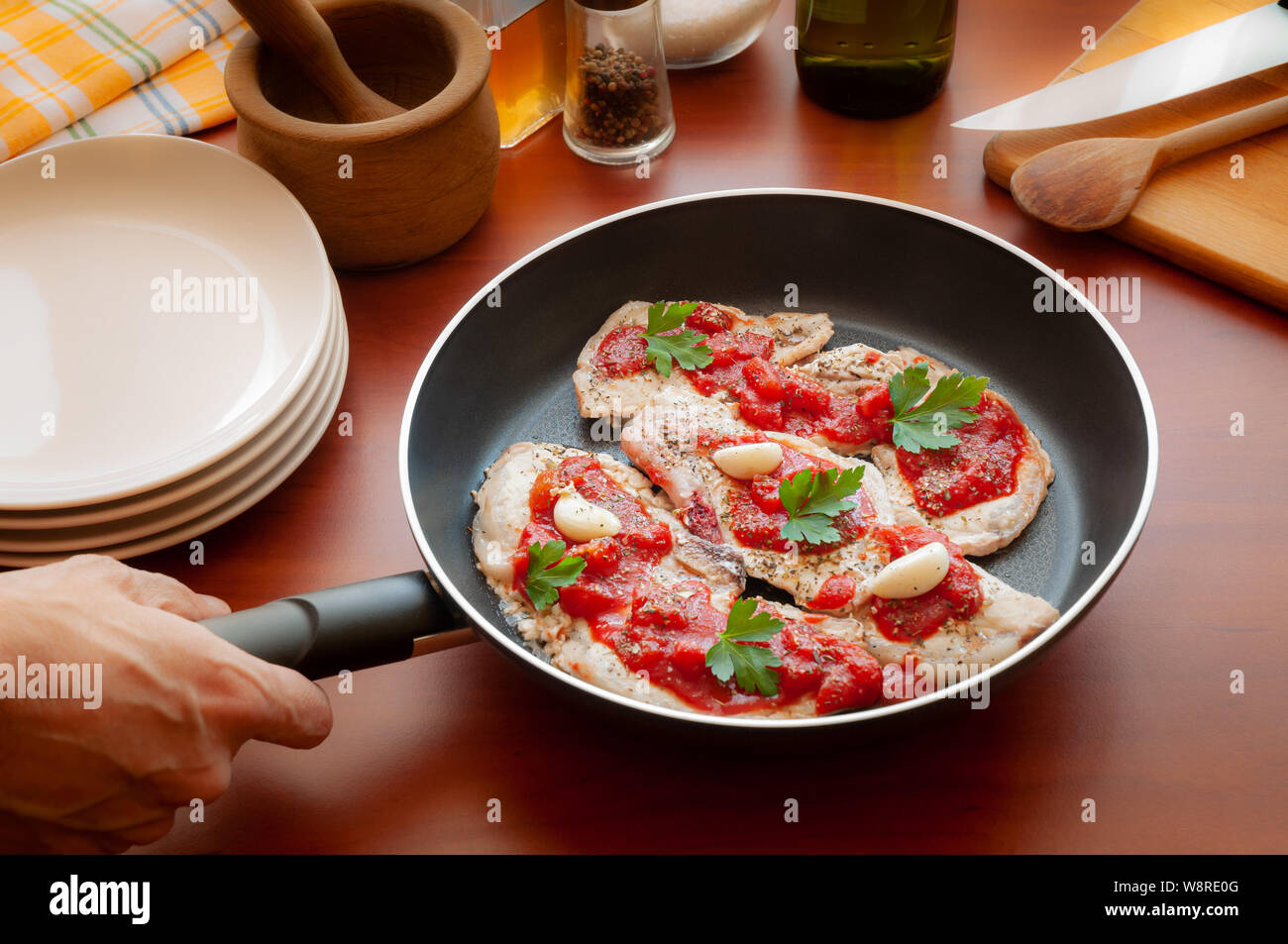 Preparazione di costolette di maiale con pomodoro, aglio, prezzemolo, olio di oliva e pepe in una padella Foto Stock