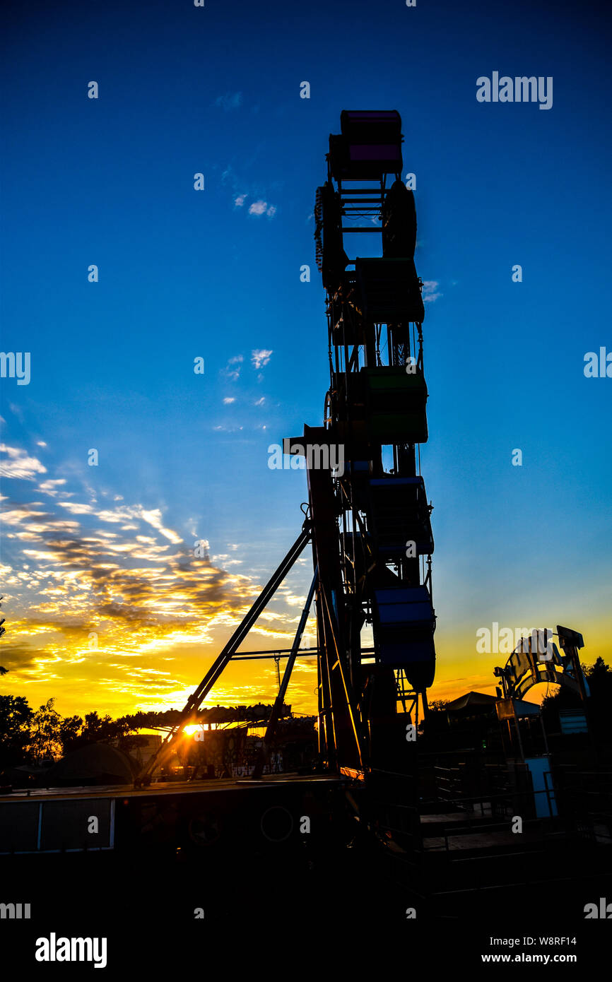 La mattina presto bagliore dorato a fiera del divertimento con grande silhouette, drammatica del cielo e una selezione di corse contro l'orizzonte Foto Stock