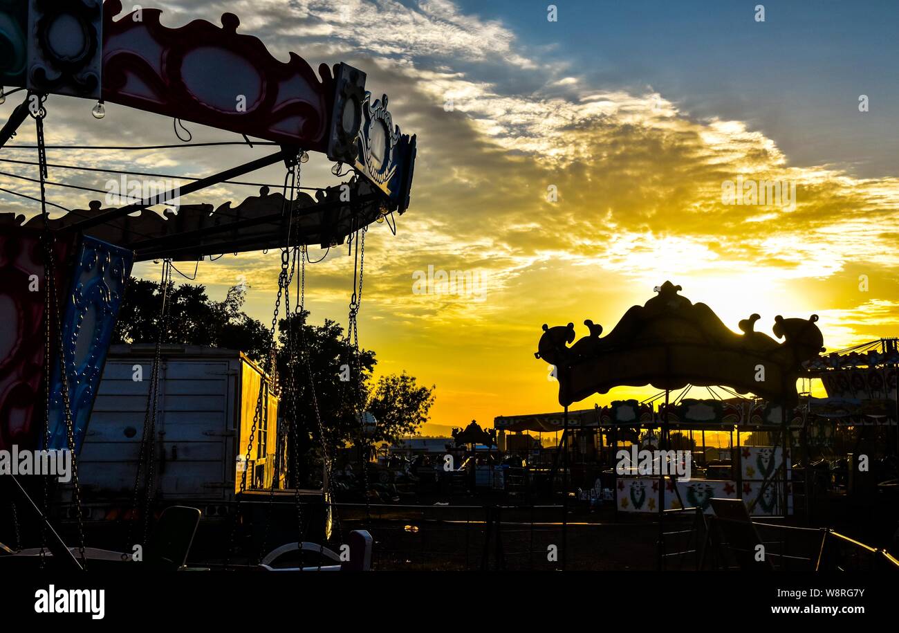 La mattina presto bagliore dorato a fiera del divertimento con grande silhouette, drammatica del cielo e una selezione di corse contro l'orizzonte Foto Stock