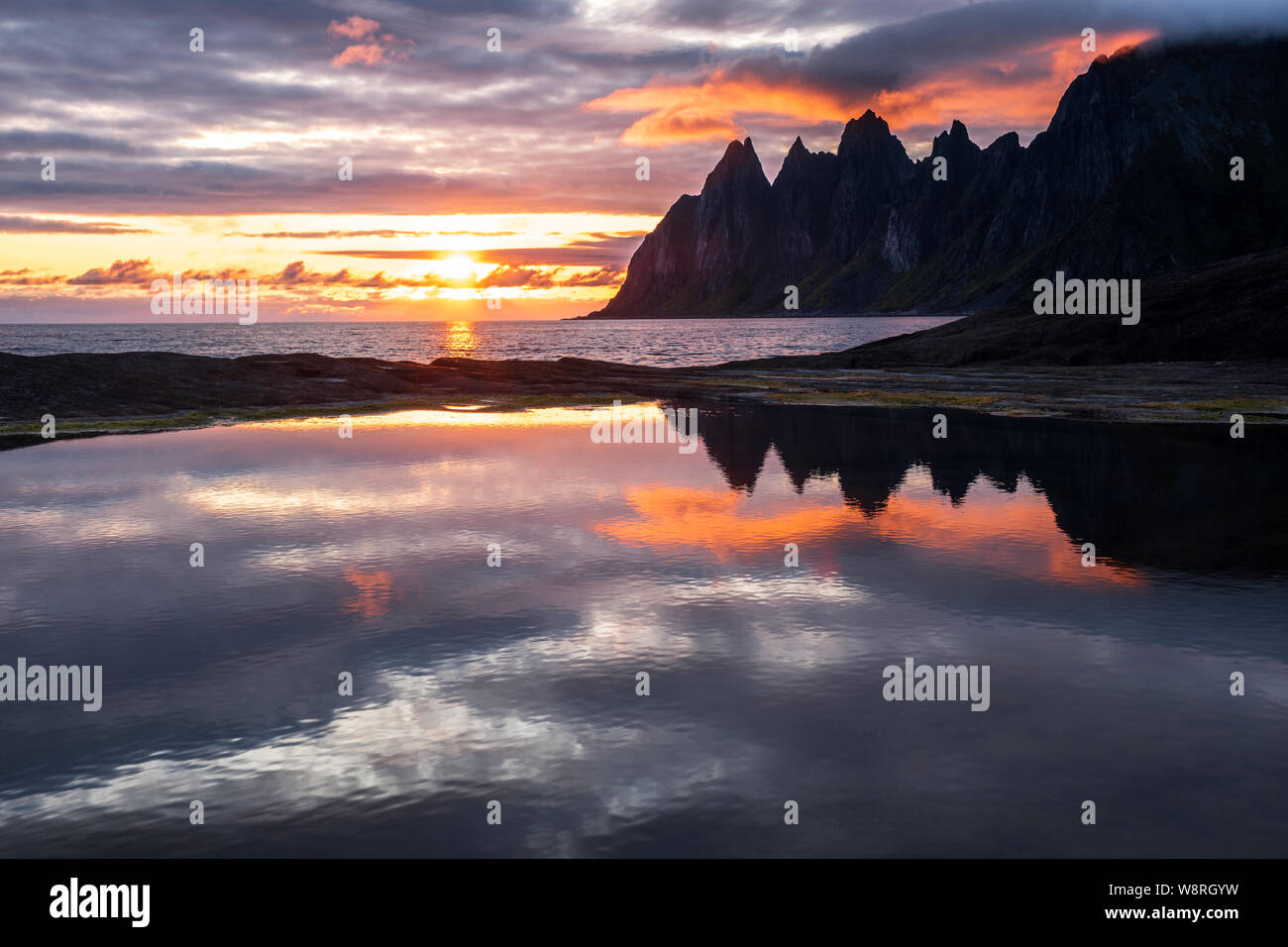 La riflessione in un rockpool impressionante di Oksen Mountain Range a molto colorato tramonto, Tungeneset, Senja, Norvegia Foto Stock
