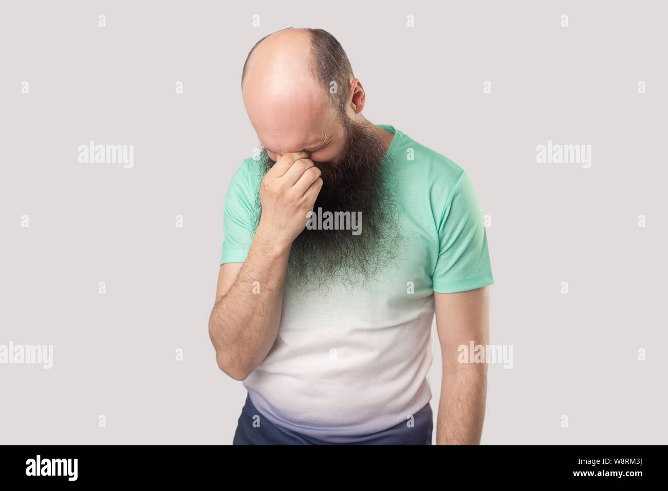 Ritratto di sola sad premuto Centro di età compresa tra uomo calvo con barba lunga in verde chiaro t-shirt in piedi tenendo la sua testa in basso e pianto. piscina studio s Foto Stock