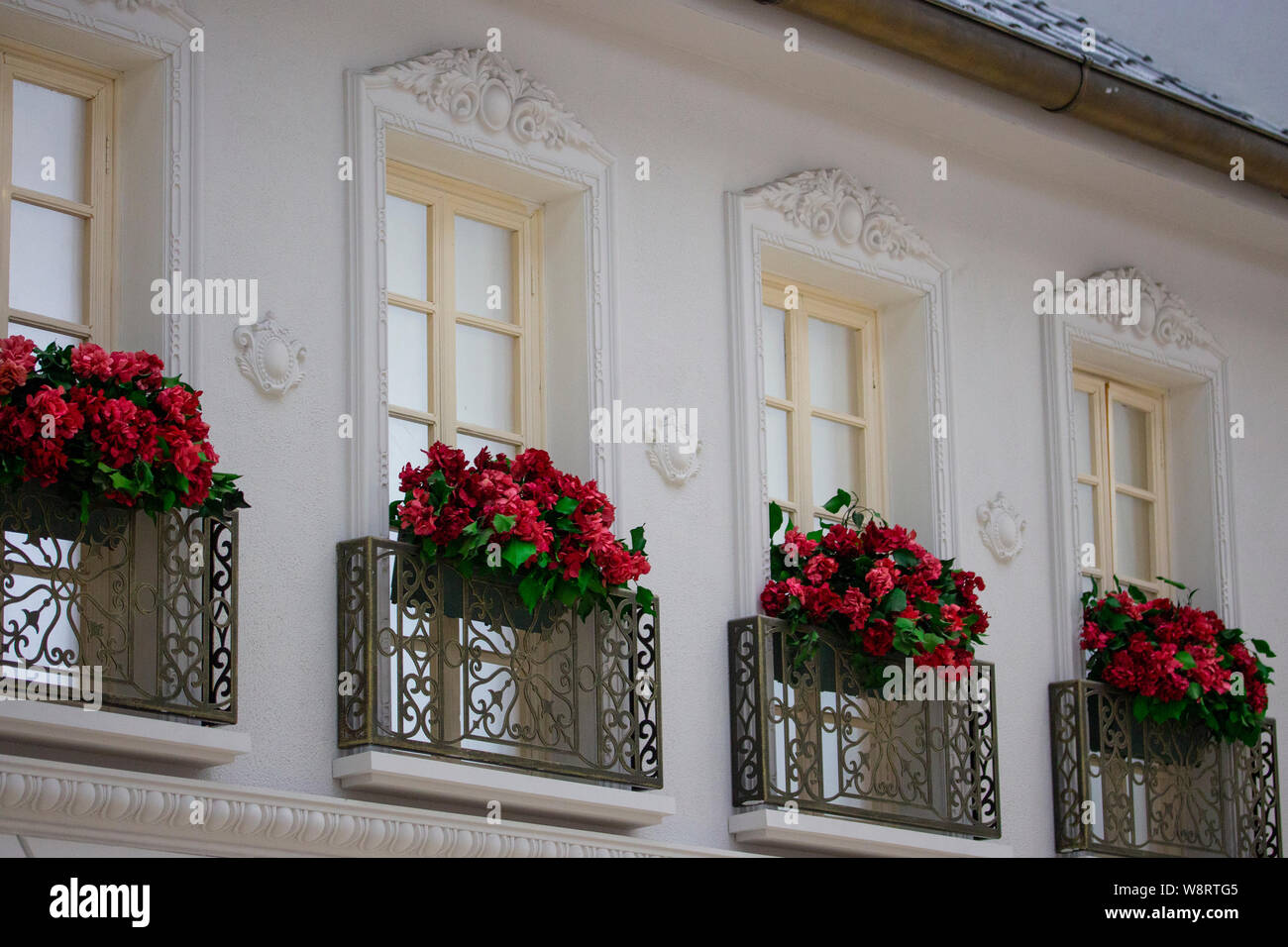 Bella alte finestre con cornici bianche e rosse balconi in ferro battuto. Stampaggio e decorazioni su una parete bianca Foto Stock