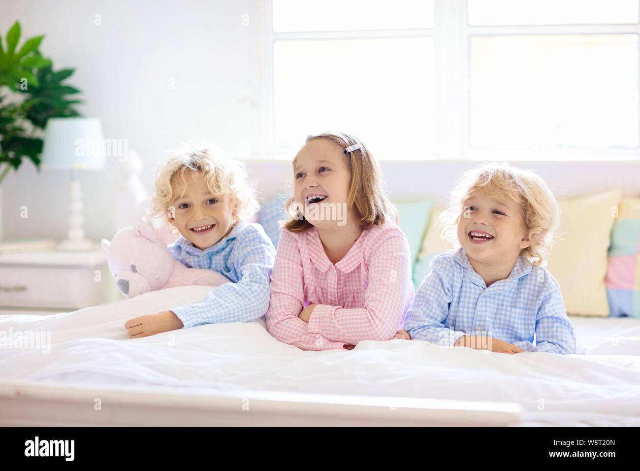 Bambini giocano a letto. I bambini a casa in bianco e luminosa camera da letto. Fratello e Sorella in abbinamento pigiami giocando in camera con i genitori. Mattina in famiglia. Ragazzo e Foto Stock