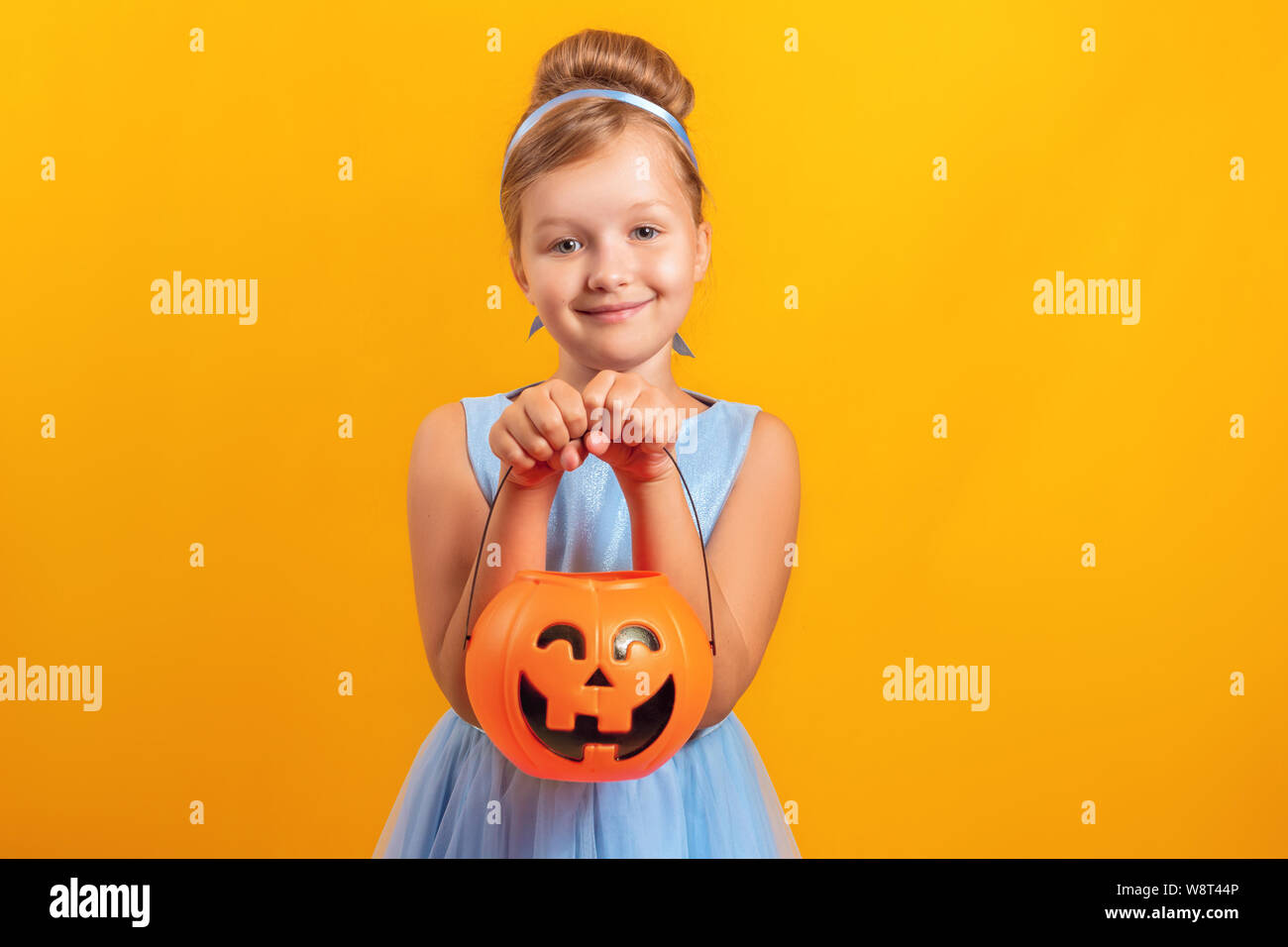 Festa di Halloween. Bambina vestito come Cenerentola su sfondo giallo. Un bambino tiene una benna di zucca lanterna di jack. Foto Stock