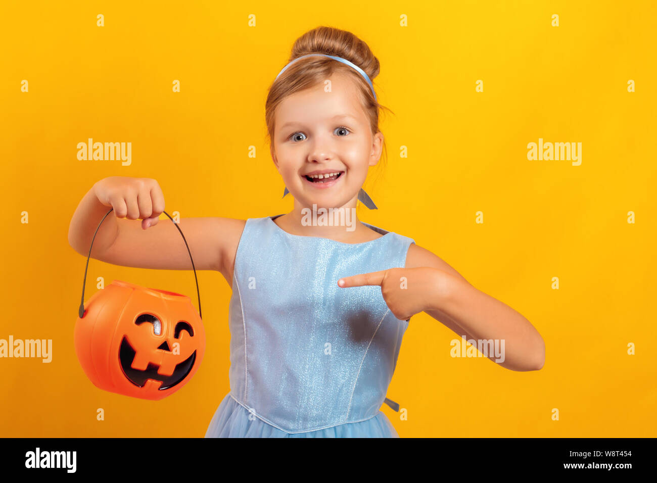 Festa di Halloween. Bambina vestito come Cenerentola su sfondo giallo. Il bambino tiene una benna di jack lanterna e punti il dito contro la zucca Foto Stock