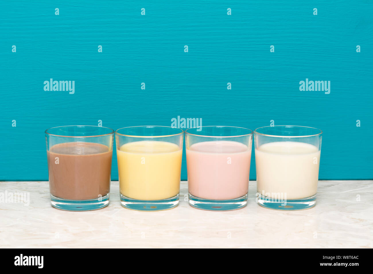 Cioccolato, banana e fragola frappè e latte fresco in bicchieri di vetro contro un sfondo teal Foto Stock