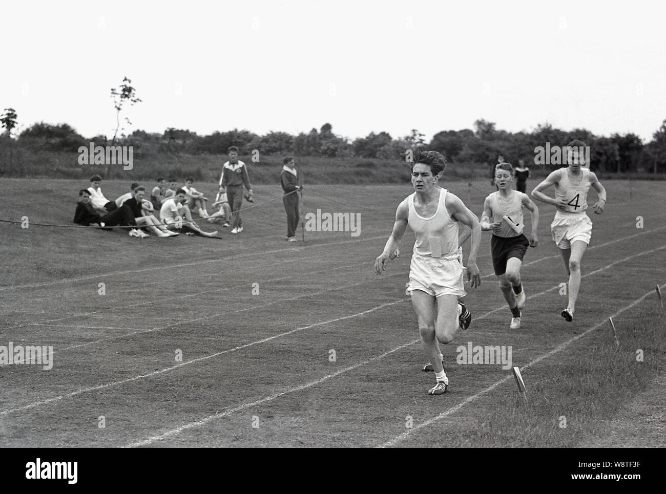 Degli anni Cinquanta, storico dilettante atleti maschili in esecuzione all'esterno in una gara su una pista in erba, Inghilterra, Regno Unito. Foto Stock