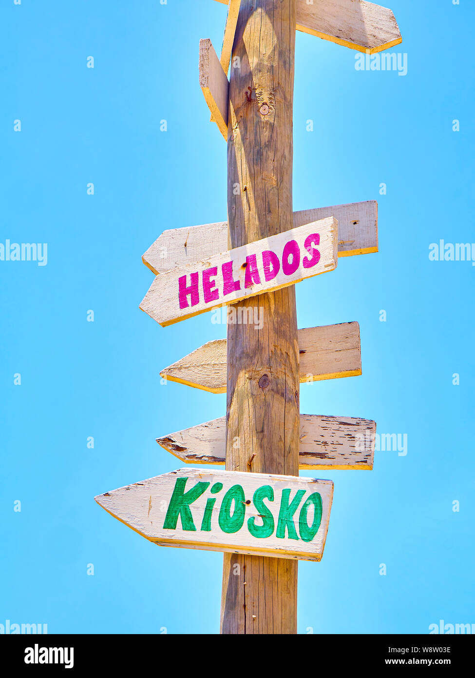 Alte Post con colorati cartelli di legno rivolta verso varie destinazioni e un servizio spiaggia in spagnolo su un cielo blu. Chiosco e gelati. Foto Stock