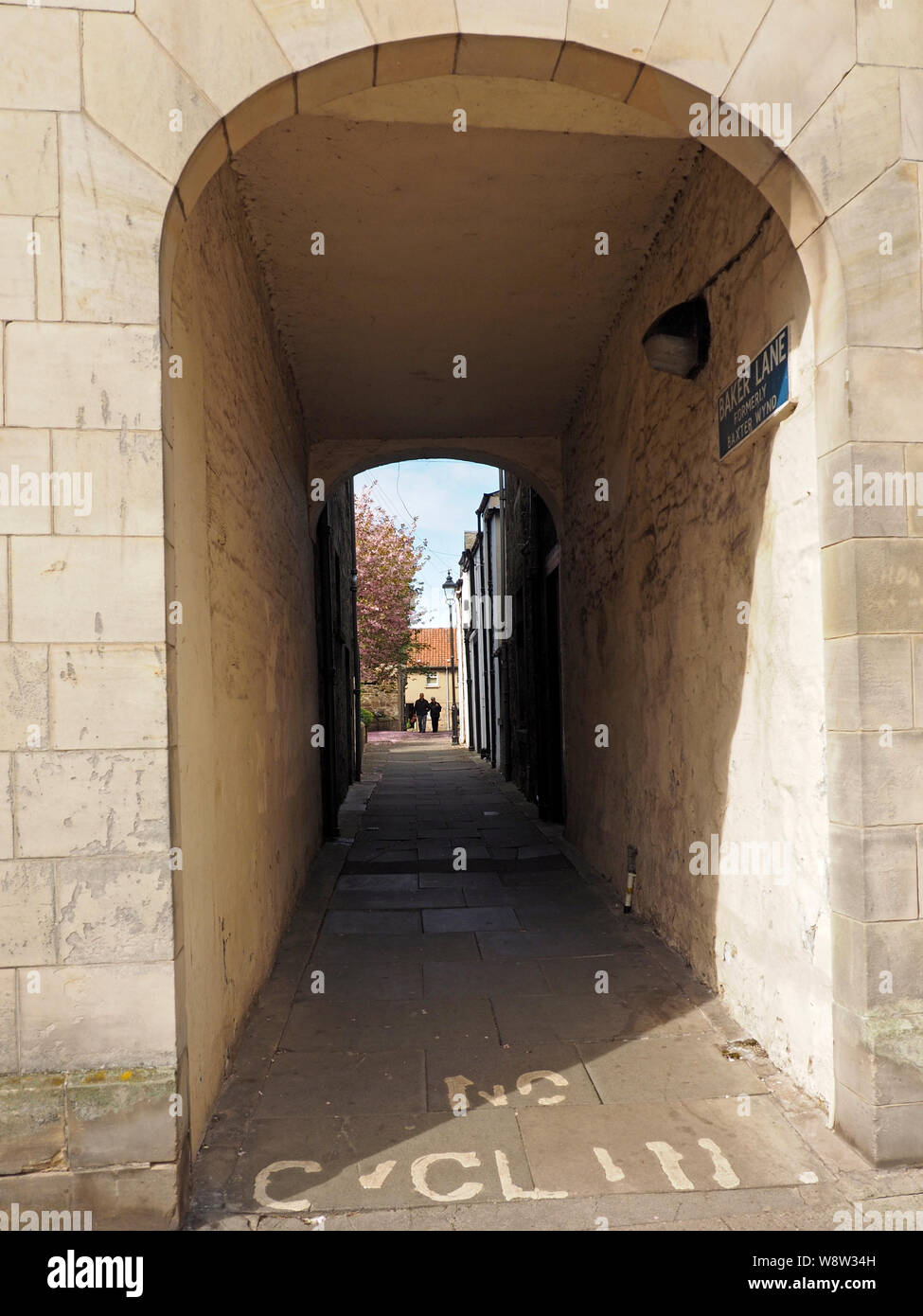 Ingresso ad arco al vialetto pedonale tra gli edifici in St Andrews Fife, Scozia con distante blossom tree e cielo blu al di là delle ombre Foto Stock
