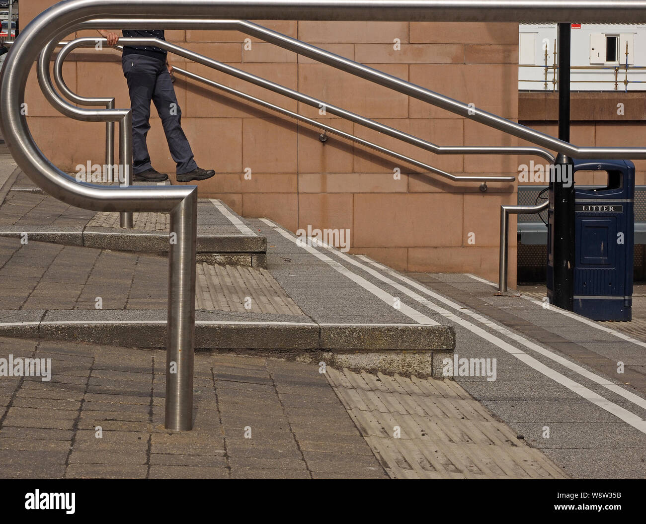 La figura passeggiando per le fasi in mezzo moderno lucido curvo in acciaio inox ringhiere in un campus in Scozia, Regno Unito Foto Stock
