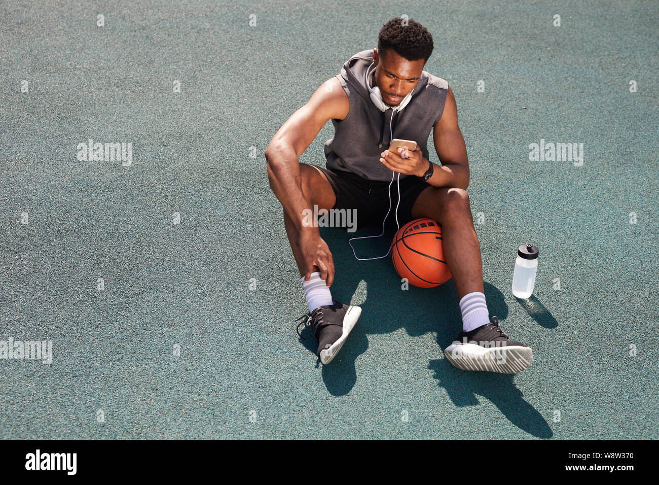 Al di sopra di vista sullo sfondo di un bel afro-americano di uomo seduto in un campo da pallacanestro e utilizza lo smartphone, spazio di copia Foto Stock