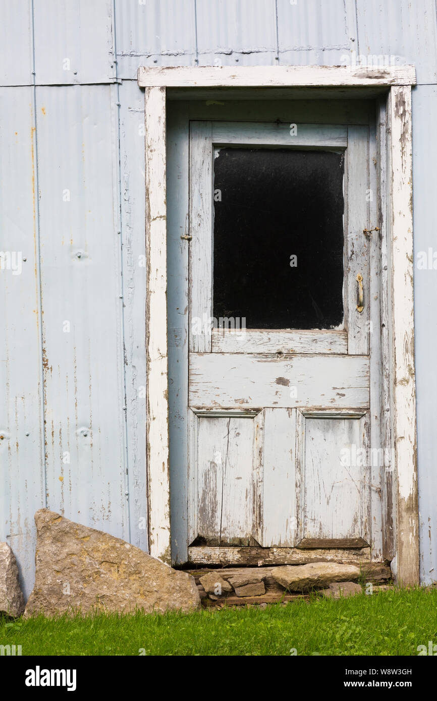 Vecchio storto in legno grigio porta di ingresso sulla lamiera ondulata edificio rivestito in cortile residenziale Foto Stock