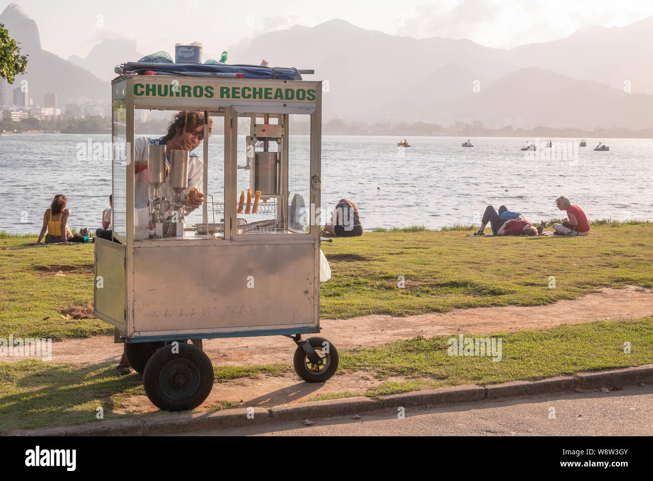 Rio de Janeiro, Brasile - 11 agosto 2019: un lavoratore vendere churros, una sorta di piede veloce, alle persone la relaxina su un parco a Rio de Janeiro, la Lagoa Rodr Foto Stock