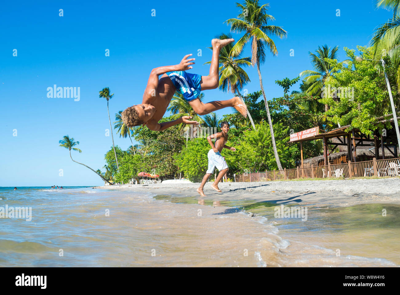 BAHIA, Brasile - Marzo 2018: i giovani brasiliani si alternano facendo capriole e acrobatico si tuffa nel mare sulla riva di un remoto villaggio spiaggia. Foto Stock