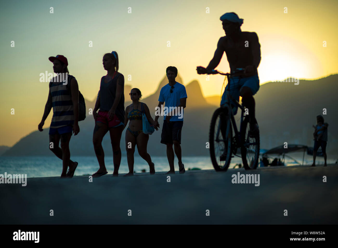RIO DE JANEIRO - Febbraio 08, 2018: i pedoni e i ciclisti condividono l'Ipanema lungomare come il sole tramonta dietro i due fratelli Montagna. Foto Stock
