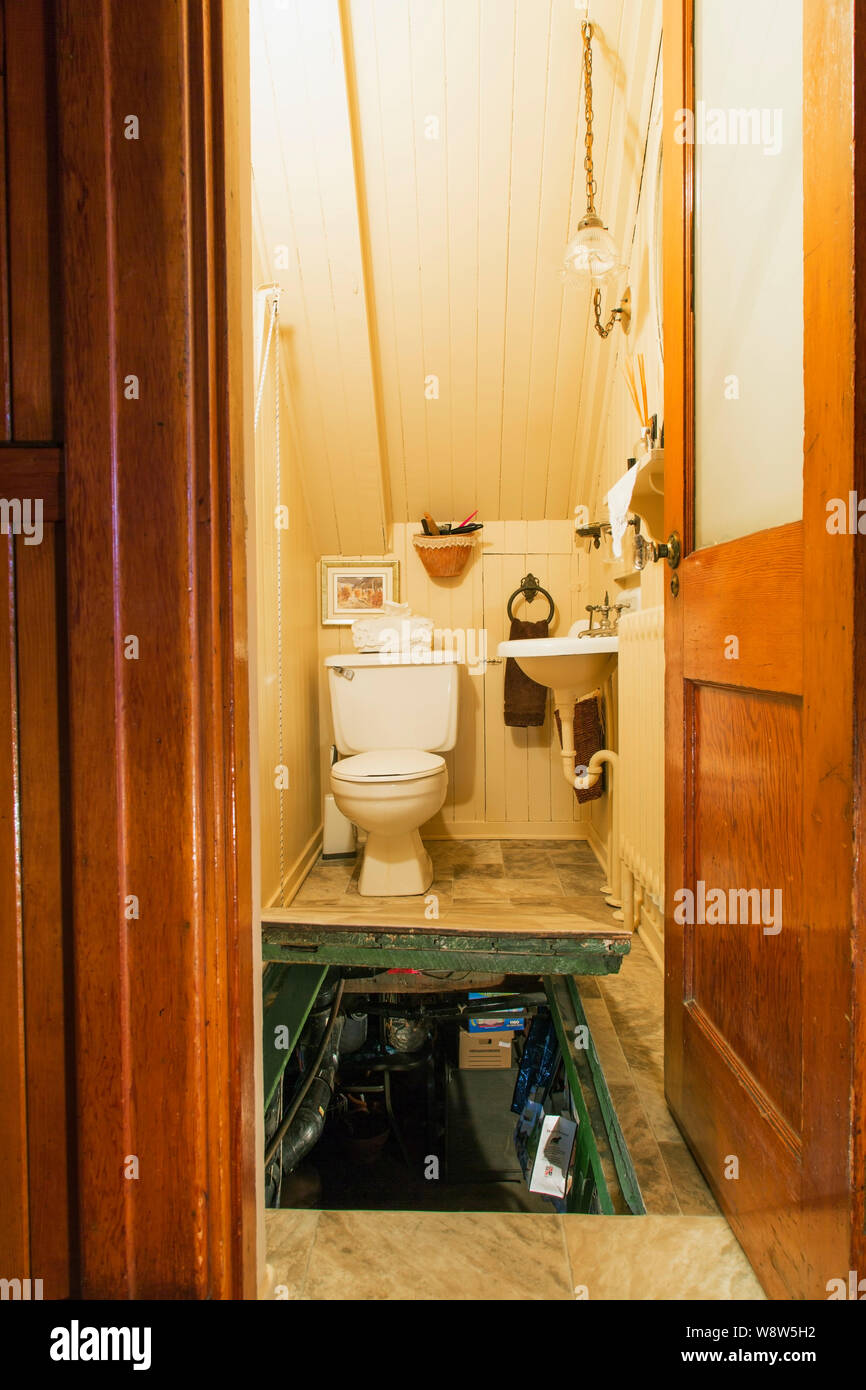 Water closet bianco con wc e lavandino, più aperto trappola porta che conduce al seminterrato sala lavanderia all'interno di un vecchio 1927 American quattro piazze house Foto Stock