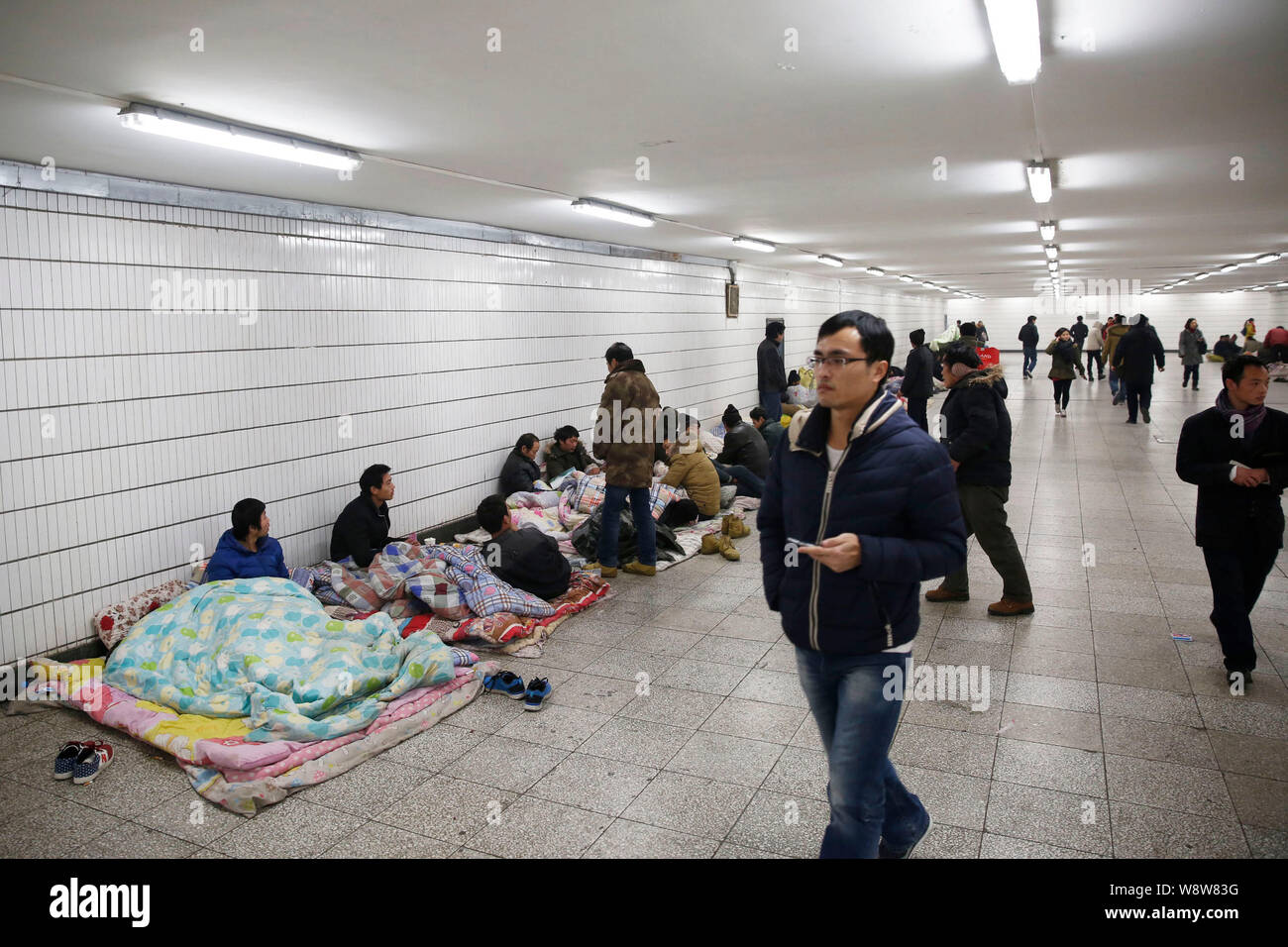 Un passeggero passeggiate passato i lavoratori migranti raccogliendo in un passaggio sotterraneo della Chaoyangmen Stazione della Metropolitana dopo che non è riuscito a ottenere i loro stipendi in Foto Stock