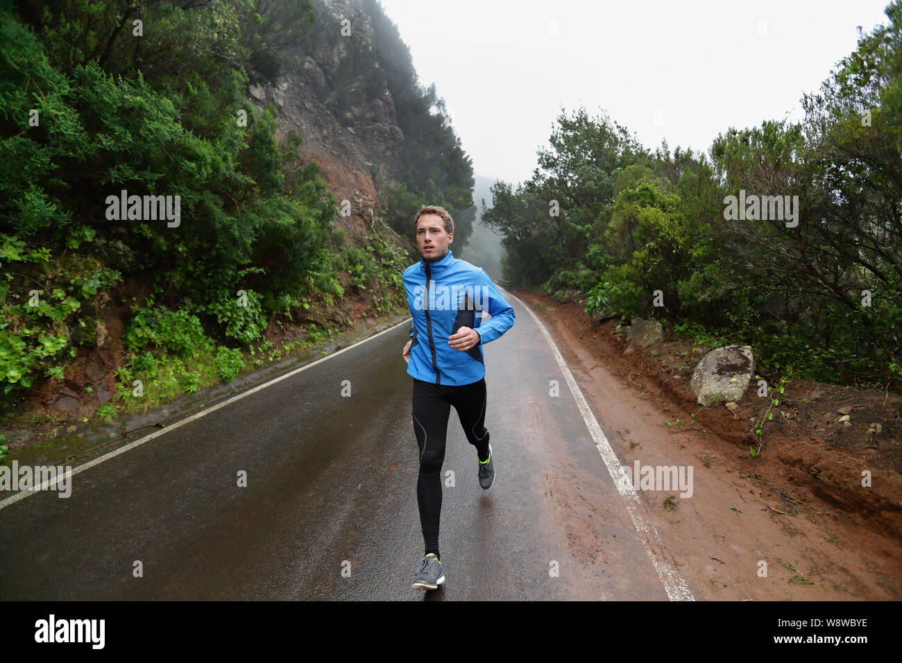 Runner maschio jogging e in esecuzione su strada in pioggia in giacca lunga e collant. Montare il modello fitness uomo che lavora fuori vivere uno stile di vita sano allenamento per la maratona. Giovani modello caucasica nel suo 20s. Foto Stock