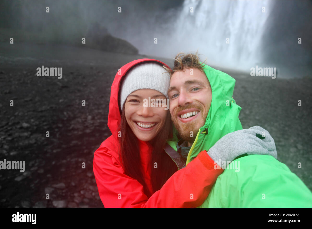 Selfie giovane prendendo immagini dello smartphone di cascata all'aperto di fronte Skogafoss in Islanda. Paio di visitare famose attrazioni turistiche e punti di interesse in natura Islandese in orizzontale sul Ring Road. Foto Stock