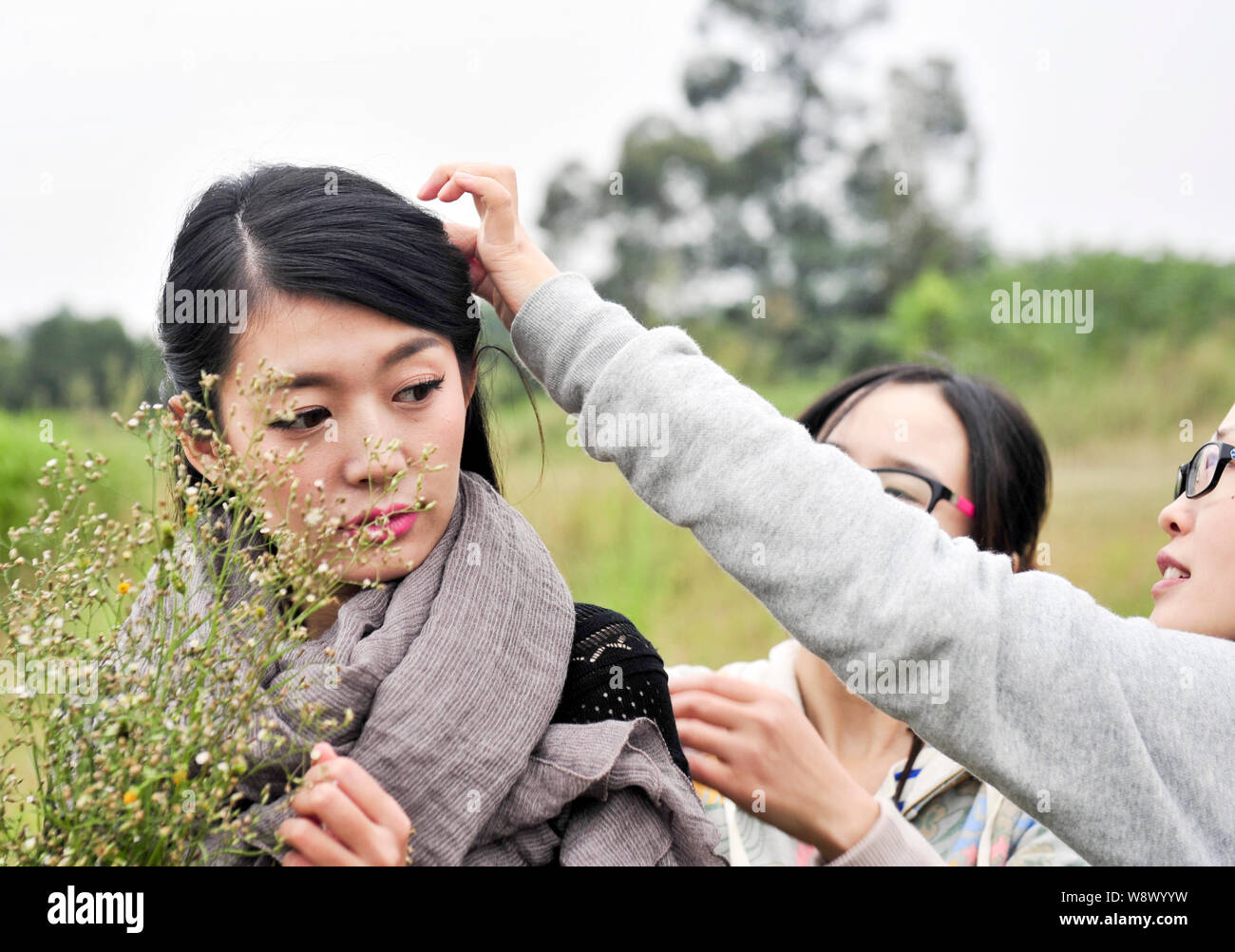 Un assistente, destro, modello aiuta Xiao Ya per regolare i suoi capelli durante una sessione di fotografia per un indumento online shop di Chengdu, a sud-ovest della Cina di Foto Stock